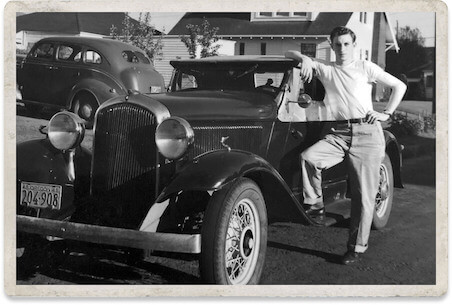 A young man leaning on his vintage car in a nostalgic old photograph
